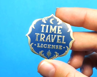 May include: A gold and blue enamel pin with the text "TIME TRAVEL LICENSE" in gold lettering. The pin has a crescent moon and star design.