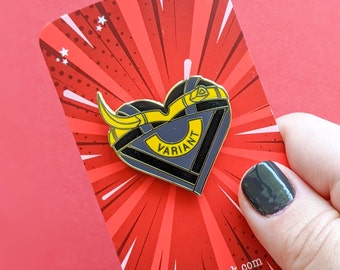 May include: A black and yellow enamel pin in the shape of a heart with the word "VARIANT" inside. The pin is on a red and white background with a comic book style design. The background also has the text "kitcronk.com".