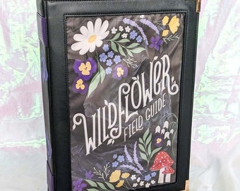 May include: A black leather-bound book with a clear plastic cover featuring a floral design and the text "Wildflower Field Guide".