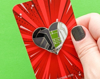 May include: A silver heart-shaped pin with a black and green design on a red background with white stars. The pin is on a card with the text "kitcronk.com".