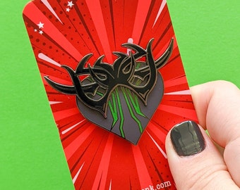 May include: Black and green enamel pin in the shape of a heart with a creature design. The pin is on a red and white background with a white star pattern. The text "kitcronk.com" is on the bottom right corner of the card.