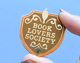 May include: Gold and orange enamel pin shaped like a shield with the text "Book Lovers Society" inside.