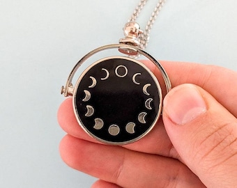 May include: A silver necklace with a black spinning pendant featuring a circle of silver crescent moons and a full moon.