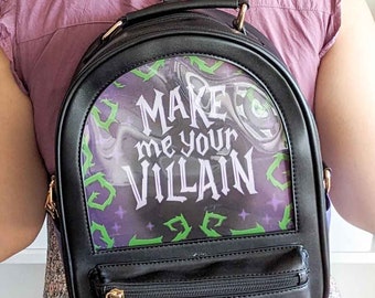 May include: Black backpack with a clear plastic panel on the front. The panel has a purple and green design with the text "Make me your Villain".