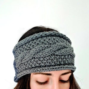 May include: A gray knitted headband with a cable knit pattern. The headband is worn by a person with brown hair.