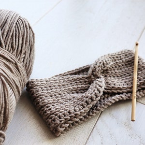 May include: A ball of beige yarn and a crocheted headband with a wooden crochet hook.