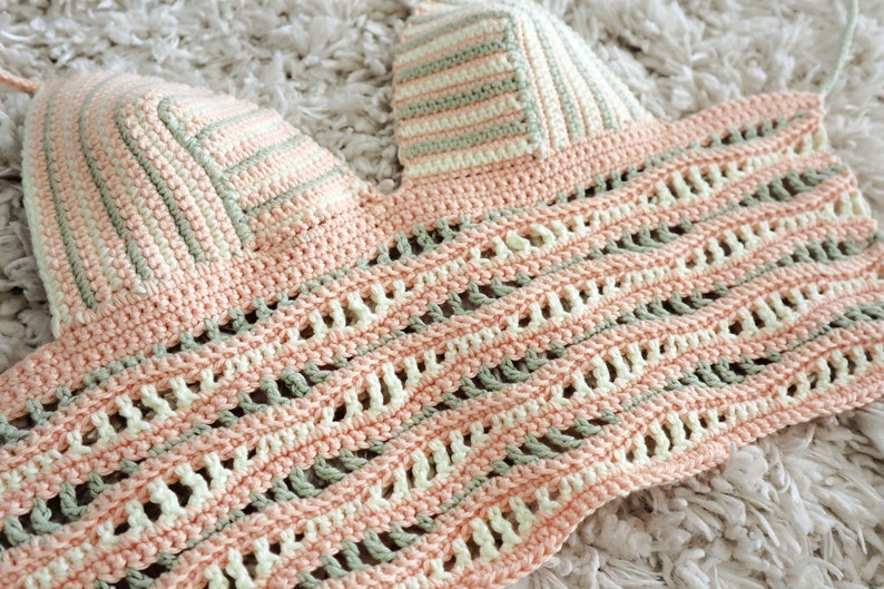 Puede incluir: Un top de crochet con un delicado dise&ntilde;o de tejido abierto en tonos rosa, verde y blanco. El top presenta un escote triangular y una longitud recortada.