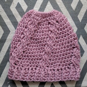 May include: A pink crocheted beanie hat with a cable knit pattern.