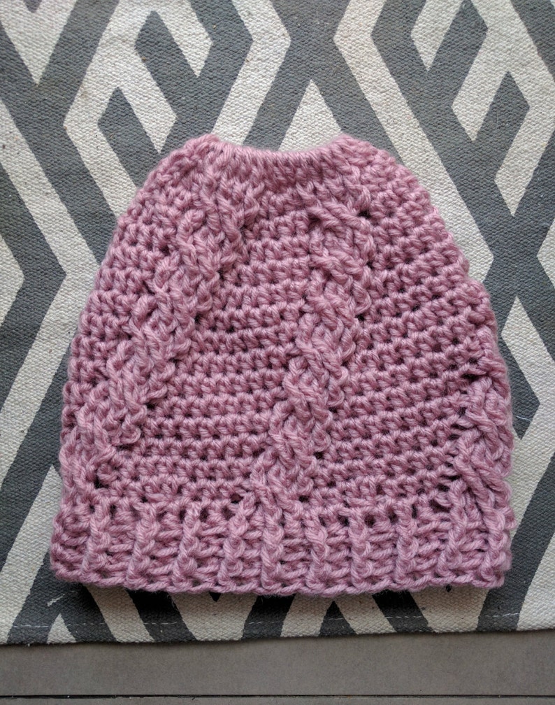 May include: A pink crocheted beanie hat with a cable knit pattern.