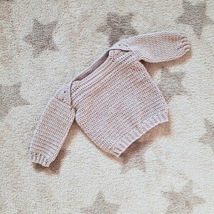 Puede incluir: Un jersey de beb&eacute; de punto de ganchillo de color rosa p&aacute;lido con mangas largas.