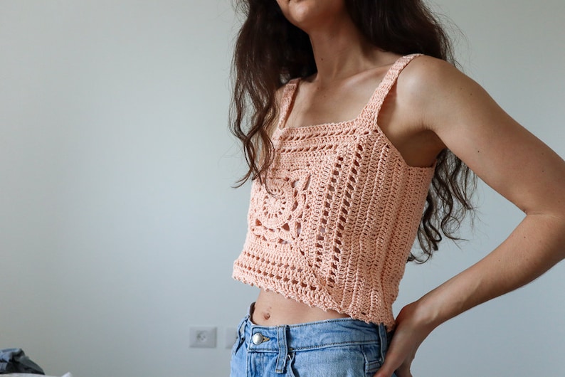 May include: A peach-coloured crochet top with a square neckline and a crocheted design. The top is cropped and has thin straps.