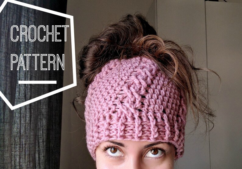 May include: A pink crocheted headband with a textured pattern. The headband is worn by a person with brown hair.