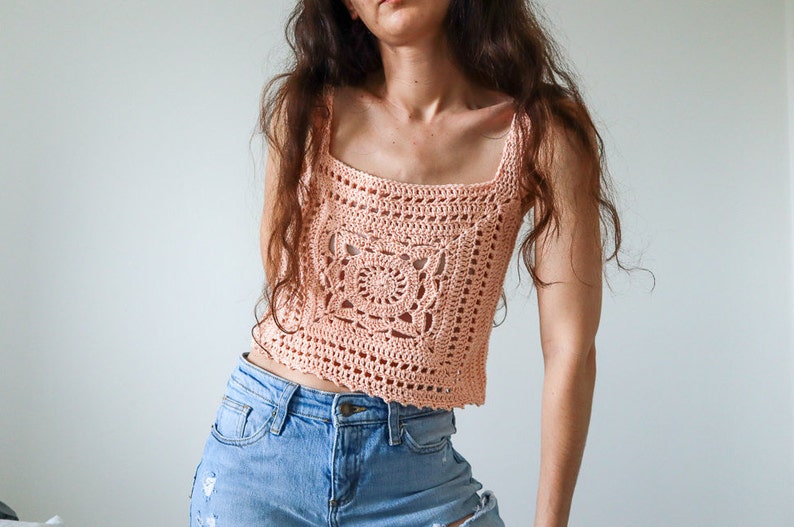 May include: A peach-coloured crochet top with a square design and a scalloped hem.
