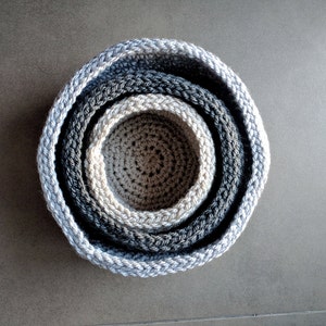 May include: Set of four gray crocheted bowls, nested inside each other. The bowls are made of a soft, textured yarn and have a subtle ombre effect.
