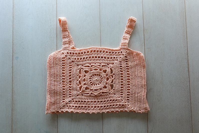 May include: A peach-coloured crochet top with a square design and a floral pattern in the centre.