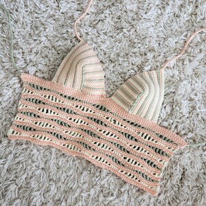 Puede incluir: Un top de halter tejido a crochet con un patr&oacute;n de rayas rosa, verde y blanco. El top tiene un escote amplio y abierto y un ajuste holgado.