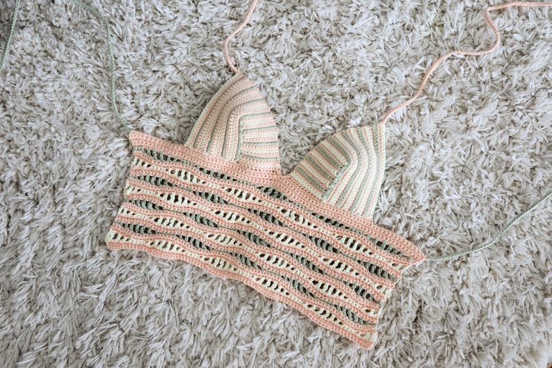 Puede incluir: Un top de halter tejido a crochet con un patr&oacute;n de rayas rosa, verde y blanco. El top tiene un escote amplio y abierto y un ajuste holgado.