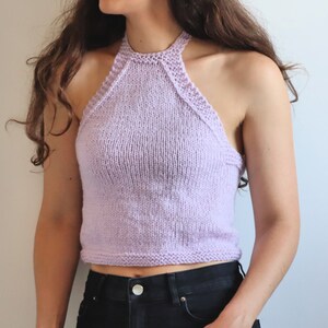 Puede incluir: Un top halter de punto de color lavanda con una longitud recortada. El top es sin mangas y tiene un diseño sencillo.