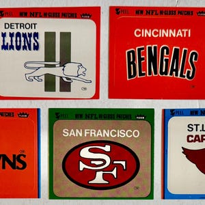 May include: A collection of vintage NFL team logo stickers. The stickers feature the logos of the New York Giants, Detroit Lions, Cincinnati Bengals, New York Jets, Cleveland Browns, San Francisco 49ers, and St. Louis Cardinals.