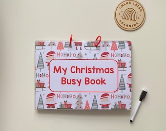 Può includere: Un libro di attività a tema natalizio rosso e bianco con il titolo "My Christmas Busy Book" sulla copertina. La copertina presenta un motivo ripetitivo di alberi di Natale, regali e Babbo Natale.