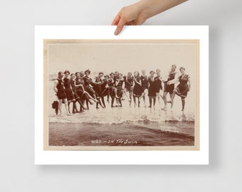 May include: A vintage black and white photograph of a group of people in bathing suits standing in the water at the beach. The photo is titled "Girls in the Swim".