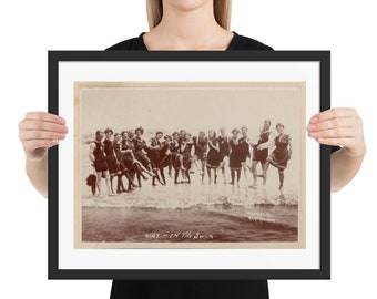 May include: A vintage black and white photograph of a group of people in bathing suits standing in the water. The photo is framed in a black frame and has the text "Girls in the Swim" printed below the image.