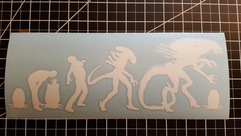 May include: White vinyl sticker depicting the evolution of the Xenomorph from the Alien franchise. The sticker shows the creature in various stages of development, from a small egg to a fully grown adult.