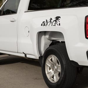 May include: White pickup truck with a black silhouette sticker of the evolution of a human to an alien on the back.