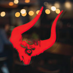 Puede incluir: Un letrero de neón rojo de una cabeza de toro con cuernos, visto a través de una ventana con luces borrosas en el fondo.