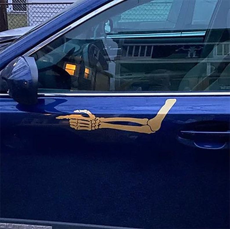 May include: A blue car with a skeleton arm pointing to the right, the arm is a gold color and is a sticker on the car.