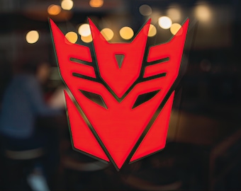 Könnte beinhalten: Ein rot-schwarzes Emblem, ein stilisiertes Symbol mit scharfen Winkeln und einem zentralen Dreieck. Das Emblem ist beleuchtet, mit einem verschwommenen Hintergrund aus warm getönten Lichtern und einem dunklen Innenraum, was auf ein Schild oder Logo hindeutet.