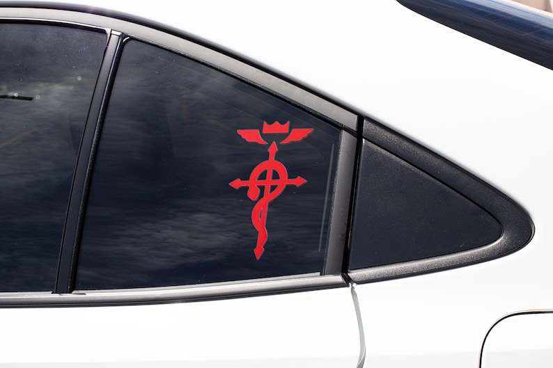 Może przedstawiać: Czerwona naklejka na szybę samochodu przedstawiająca alchemiczny symbol Kamienia Filozoficznego, krzyż z k&oacute;łkiem i wężem owiniętym wok&oacute;ł.