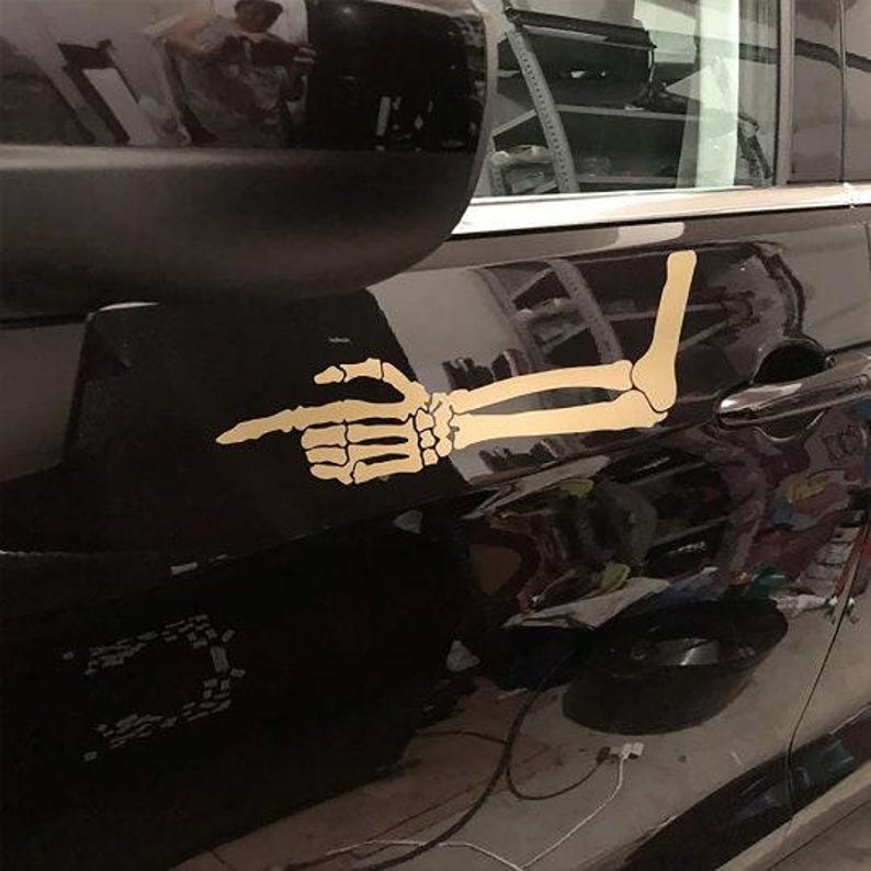 May include: A black car with a gold skeleton arm decal pointing to the right. The decal is on the side of the car, near the door handle.