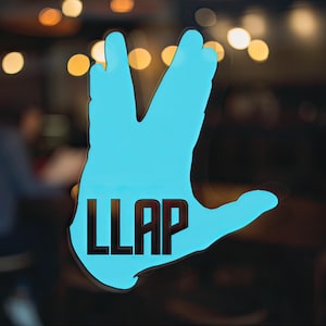 Puede incluir: Una mano azul con tres dedos levantados y el texto "LLAP" en la palma. La mano está sobre un fondo borroso.