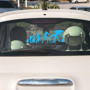May include: A white car with a blue silhouette sticker on the back window. The sticker depicts a progression of alien-like figures, starting with a small, hunched figure and ending with a large, imposing figure.