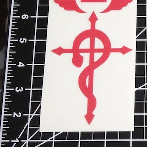 Może przedstawiać: Czerwona naklejka winylowa z alchemicznym symbolem z anime Fullmetal Alchemist. Symbol przedstawia krzyż z owiniętym wok&oacute;ł nim wężem, koroną i skrzydłami.