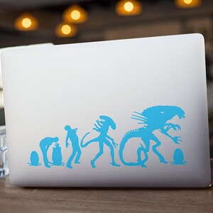 May include: A blue alien evolution sticker on a silver laptop. The sticker shows a series of aliens in different stages of development, from a small egg to a large, menacing creature.