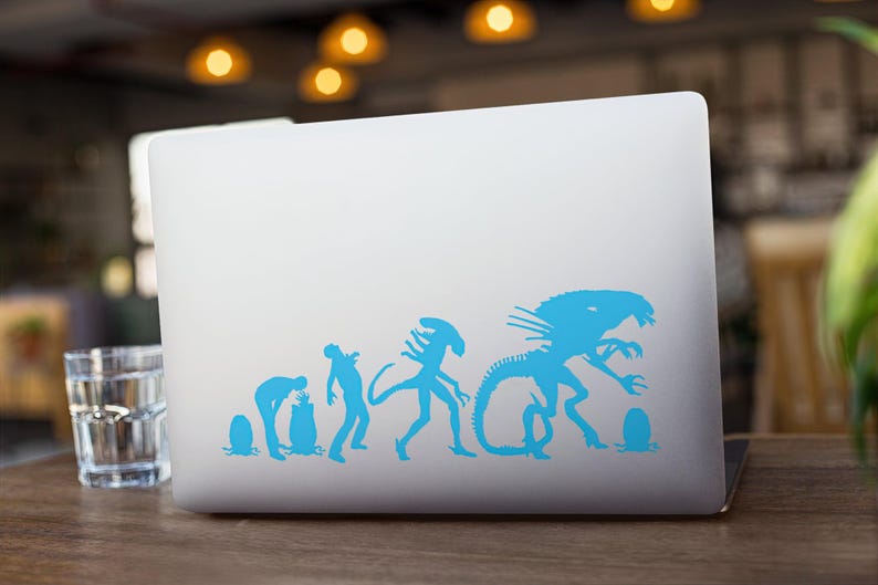 May include: A blue alien evolution sticker on a silver laptop. The sticker shows a series of aliens in different stages of development, from a small egg to a large, menacing creature.