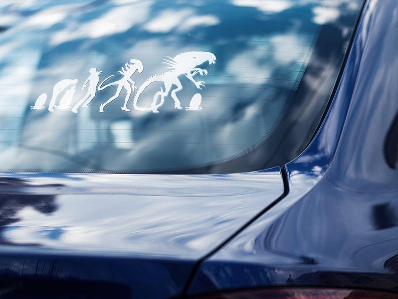 May include: A white vinyl sticker on the back window of a blue car. The sticker shows a humorous evolution of a creature from a simple organism to a Xenomorph from the Alien movie franchise.