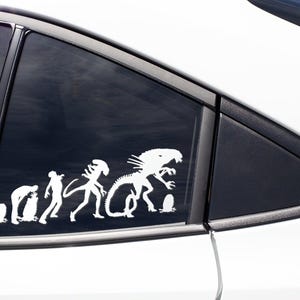 May include: A white vinyl sticker depicting the evolution of the Alien creature from the movie franchise. The sticker shows a progression from a single-celled organism to the iconic Xenomorph.