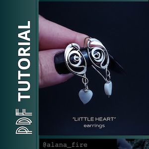 May include: Silver earrings with a distinctive design. Each earring has a swirl at the top, a small heart-shaped charm, and a small, oblong bead. The text "LiTTLE HEART" earrings is visible.