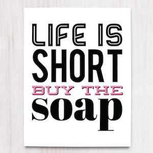 May include: Black and white typography print with the text "Life is short buy the soap" in a bold font. The word "buy" is in pink.