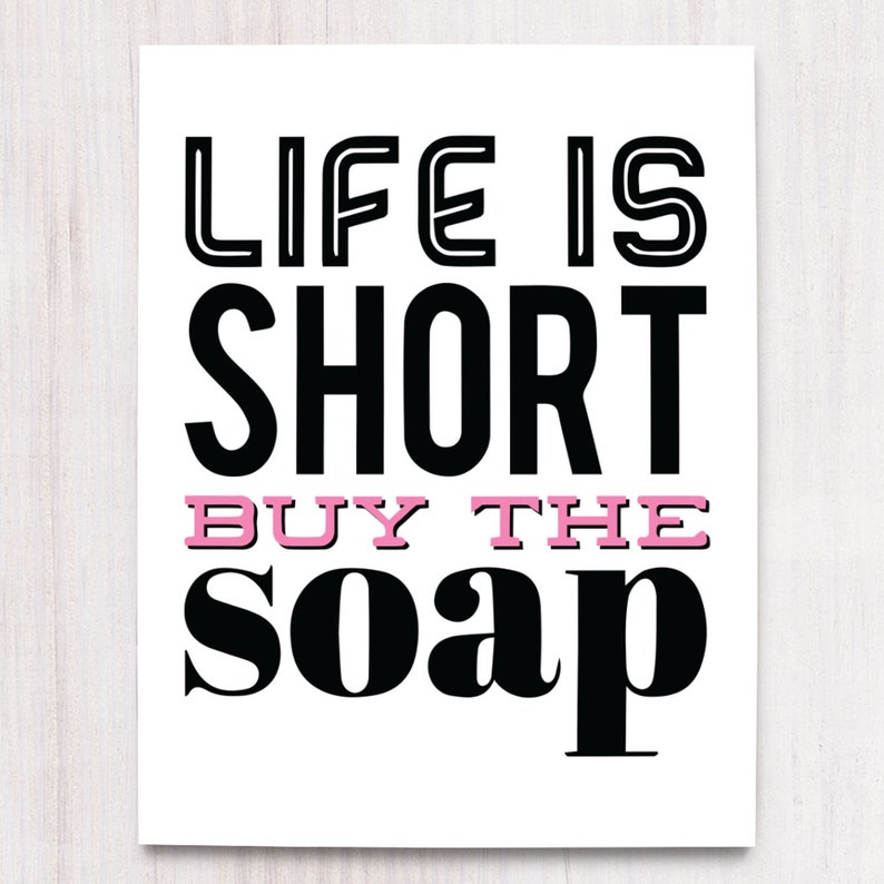 May include: Black and white typography print with the text "Life is short buy the soap" in a bold font. The word "buy" is in pink.