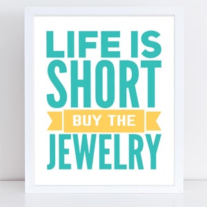 May include: White framed print with the text "Life is short buy the jewelry" in teal blue and yellow.