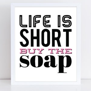 May include: Black and white typography print with the text "Life is short buy the soap" in a bold font. The word "buy" is in pink.
