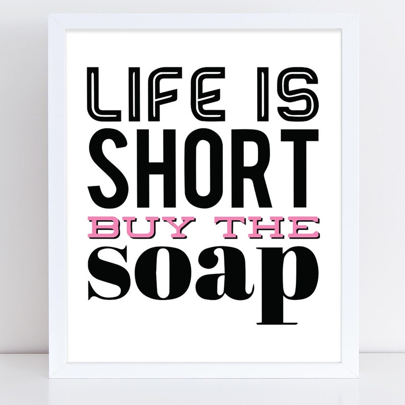 May include: Black and white typography print with the text "Life is short buy the soap" in a bold font. The word "buy" is in pink.