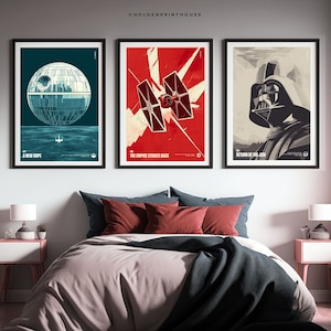 Pode incluir: Três impressões de pôsteres de filmes Star Wars em molduras pretas. Os pôsteres são de estilo minimalista com fundo vermelho, azul e bege. Os pôsteres apresentam a Estrela da Morte, um caça TIE e Darth Vader.