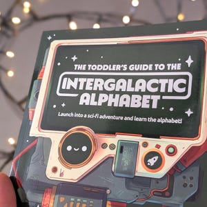 Puede incluir: Un libro infantil titulado "The Toddler's Guide to the Intergalactic Alphabet". La portada presenta un dise&ntilde;o retro-futurista con una ilustraci&oacute;n tipo robot y el texto "Launch into a sci-fi adventure and learn the alphabet!". La combinaci&oacute;n de colores incluye verde, rojo y blanco.