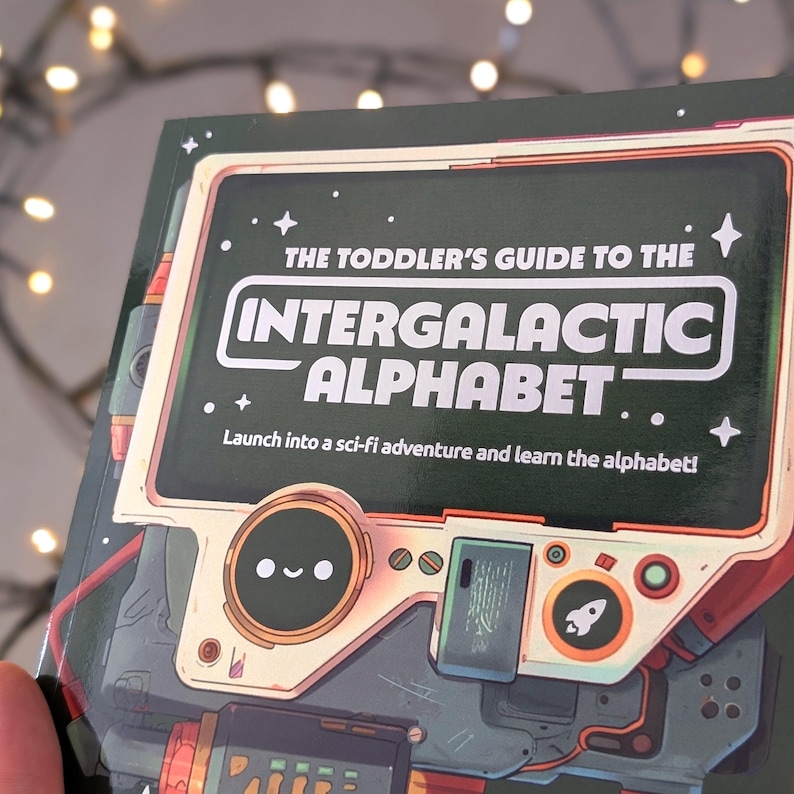 Puede incluir: Un libro infantil titulado "The Toddler's Guide to the Intergalactic Alphabet". La portada presenta un dise&ntilde;o retro-futurista con una ilustraci&oacute;n tipo robot y el texto "Launch into a sci-fi adventure and learn the alphabet!". La combinaci&oacute;n de colores incluye verde, rojo y blanco.