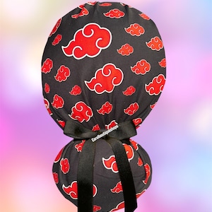 May include: Black scrub cap with a red cloud pattern and a black bow. The cap features a repeating design of red clouds with white outlines on a black background. The bow is tied at the base of the cap. The text "Carolboutiqueshops" is printed on the bow.